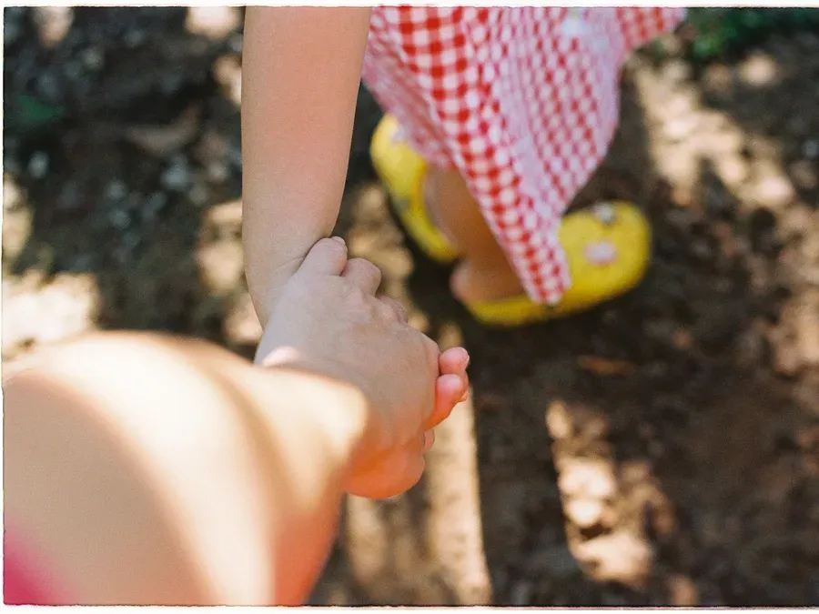 Enfant vu de dos qui marche en tenant la main d'un adulte