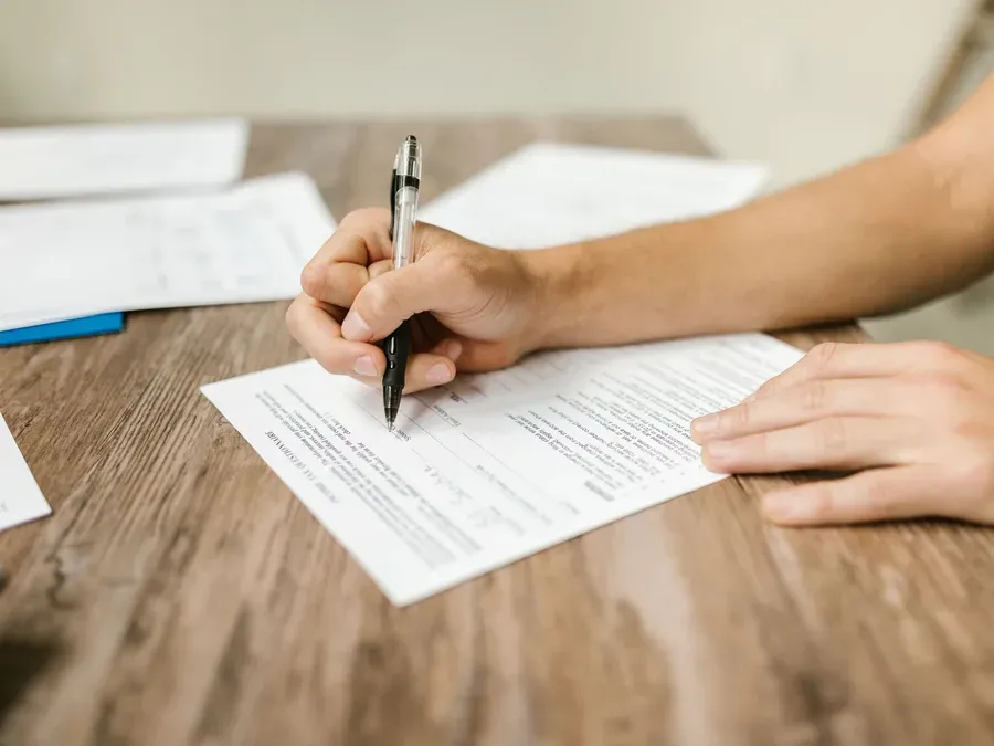 Mains qui signent un formulaire posé sur un bureau en bois