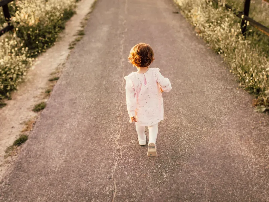 Enfant vu de dos qui marche sur un chemin bordé de fleurs des champs