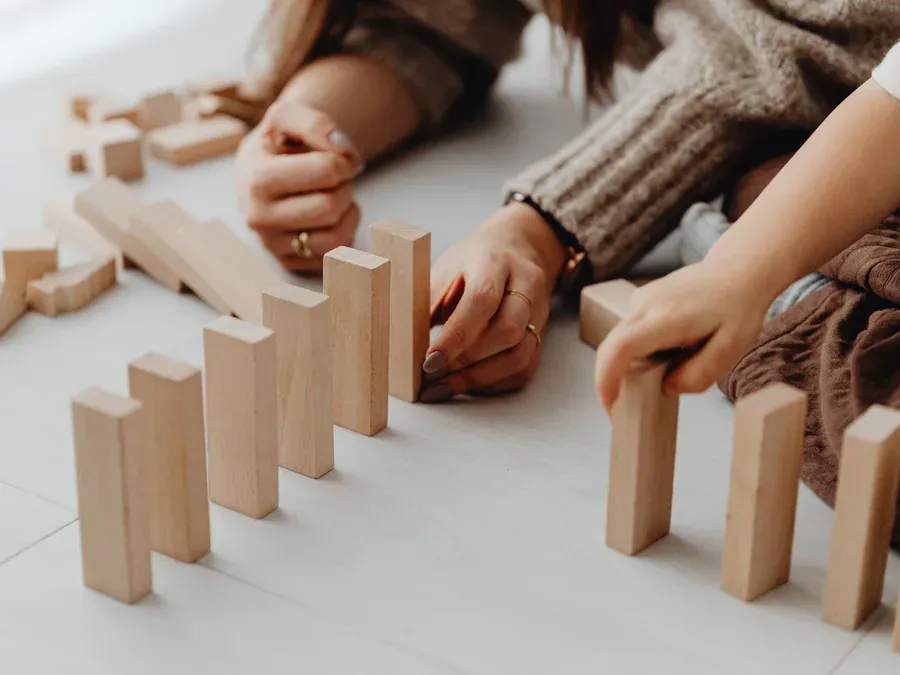 Mains d'un adulte et d'un enfant qui empilent des dominos en bois